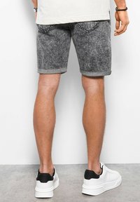 Grijze denim shorts met een gestructureerde afwerking, opgerolde zoom en achterzakken, gecombineerd met zwart-witte sneakers.