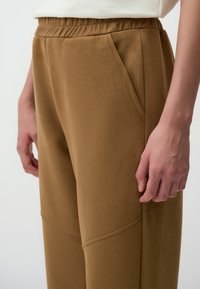 Bruine, zachte stofbroek met zijzakken. Heeft een relaxte pasvorm, een elastische tailleband en subtiele stitchdetails langs de benen.