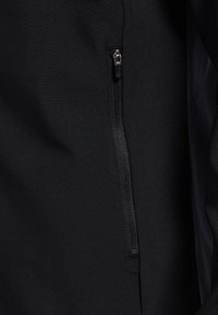 Parte de una chaqueta negra con cremallera, con una textura suave y mate. Presenta una cremallera contrastante y detalles de costura.