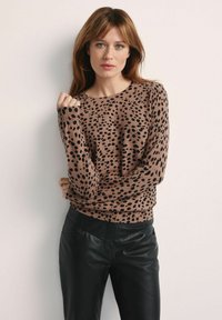 Brązowy sweter w czarny zwierzęcy wzór, okrągły dekolt, długie rękawy, ściągacze na rękawach i u dołu. W zestawieniu z czarnymi skórzanymi spodniami.