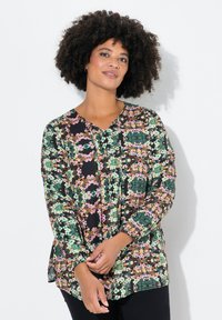 Långärmad blus med blommönster som har en svart bakgrund med gröna, rosa och gula mönster, lätt tyg, V-ringning och sprund på sidorna.