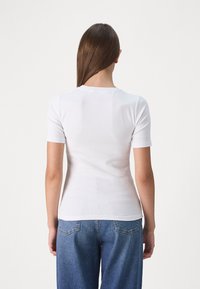 Hvit kortermet tettsittende topp med en rund hals, laget av ribbestrikket materiale, kombinert med mørkeblå høy midje jeans.