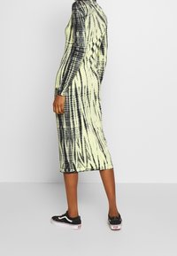 Dlouhý rukáv, šaty s tkaným vzorem v černé a neonově žluté barvě, se slim fit střihem a délkou do poloviny lýtek. Nyní nosí s černými teniskami.