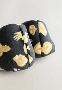 Botines de felpa negra con patrones amarillos de temática marina. Forma redondeada con una textura suave, costuras rematadas y sin hardware o acentos visibles.