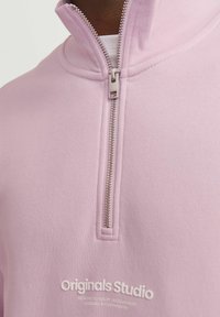 Light pink quarter-zip fleece with a smooth texture. Features a silver zipper and a white embossed logo at the bottom. Simple, modern design.