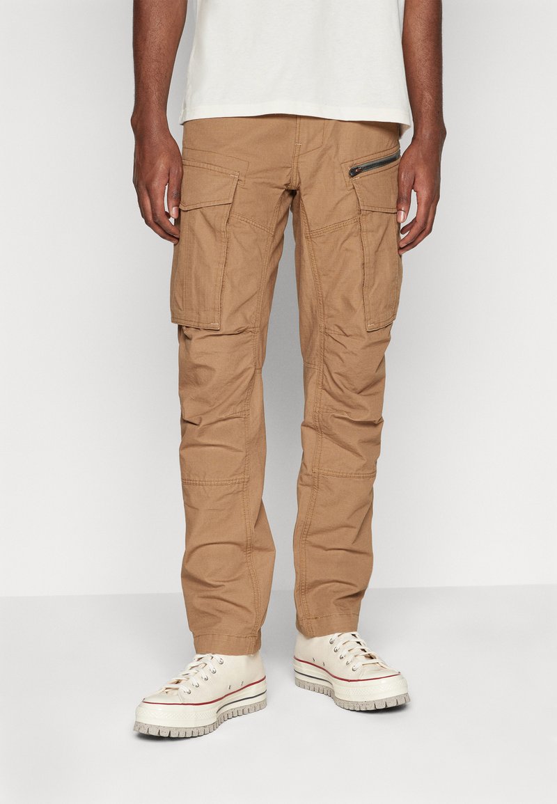 Khaki cargobroek van katoenmix met meerdere zakken, een met rits afgesloten zijzak en een taps toelopend ontwerp. G gedragen met witte sneakers.