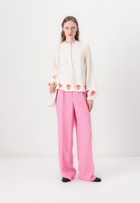 Off-white bluza s barvitim cvetličnim vezenjem na robu, kombinirana s svetlo roza širokimi hlačami. Črne čevlje dopolnjujejo videz.