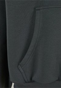 Gros plan sur la poche d'un sweat-shirt gris foncé avec des coutures visibles et un détail de bord-côte à la taille.