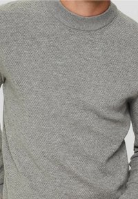 Světle šedý pletený svetr s kulatým výstřihem, texturovaným vzorem a žebrovanými manžetami. Tkanina vypadá měkce a prodyšně.