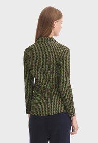 Langarmshirt met een groen en bruin zigzagpatroon, voorzien van een kraag en een gestructureerde stof, gezien vanaf de achterkant.