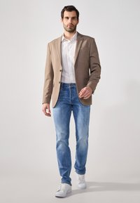 Light brown blazer over a white shirt, paired with light blue jeans and white sneakers. The blazer has a single pocket and structured fit.