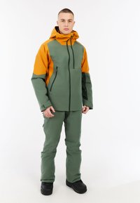 Waterdichte jas in groen en oranje, met een rits aan de voorkant, zijzakken, een verstelbare capuchon en duurzaam materiaal; gecombineerd met bijpassende broek.