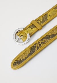 Ceinture en cuir jaune avec un motif serpent, dotée d'une boucle circulaire en argent et d'une texture lisse. Comprend des trous d'ajustement.