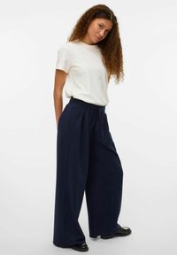 Pantaloni ampi navy con cinturino in vita regolabile, abbinati a una t-shirt bianca a collo rotondo. Tessuto morbido, vestibilità comoda e superficie liscia.