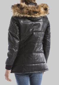 Giacca di pelle nera con dettagli trapuntati, bordo della cappuccio in pelliccia sintetica e polsini a coste. Presenta un design aderente e pannelli cuciti.