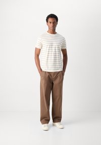 Striped short-sleeve t-shirt in off-white with brown lines, paired with loose-fitting brown trousers and white sneakers.