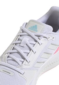 Chaussure de sport blanche avec une tige en mesh, des accents gris et une semelle rose. Comprend des lacets, un logo à trois bandes et un col rembourré.