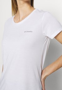 Vit kortärmad t-shirt i mjukt material, med rund hals och en liten grå Columbia-logotyp på vänster bröst.