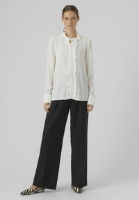 Witte blouse met gerimpeld voorpand en knoopdetails, lange mouwen, gecombineerd met zwarte wijde broek en flats met dierenprint.