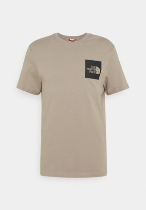 Lysebrun T-shirt med korte ærmer og rund hals med et sort firkantet logo patch fra The North Face på venstre bryst.