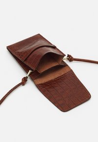 Hnědá kabelka z kůže se vzorem krokodýlí kůže, s klopou na zapínání, vnitřní přihrádkou a odnímatelným popruhem, s hladkou texturou.