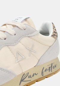 Hellbeige Sportschuhe mit einem strukturierten Obermaterial aus Wildleder und Stoff, das eine Leopardenmuster-Ferse aufweist und den Text "Schneller laufen" auf der Sohle trägt.