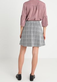 Top lila claro con mangas acampanadas; falda a cuadros gris; silueta acampanada; combinada con zapatos negros, vista desde la parte trasera.