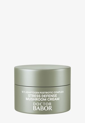 Green, round cream jar with a smooth matte finish. Label features white text: "12% Adaptogen Postbiotic Complex Stress Defense Mushroom Cream."