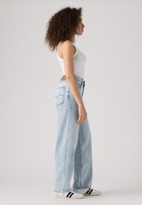 Világoskék, magasderekú egyenes szárú farmernadrág hátsó zsebbel és bőr címke részlettel. Fehér ujjatlan felső és sportcipők.