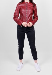 Chaqueta de cuero roja con cuello redondo, cremallera frontal y bolsillos con cremallera, combinada con jeans skinny negros y zapatillas blancas.