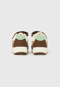 Baskets marron et crème avec des accents vert menthe, tissu texturé et forme arrondie. Vue arrière montrant un col rembourré et une semelle en caoutchouc.