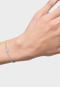 Braccialetto d'argento con un design a catena e un accento centrale a forma di lucchetto, mostrato su una mano con carnagione chiara su uno sfondo semplice.