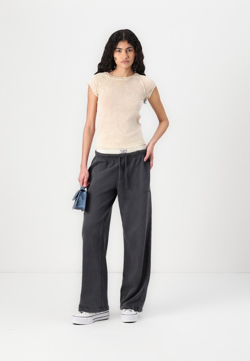 Light beige fitted t-shirt with short sleeves, paired with loose, dark gray sweatpants and white platform sneakers. Small blue handbag held in hand.