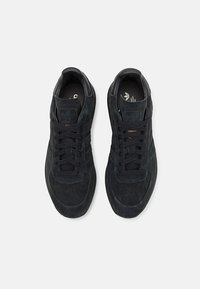 Een paar zwarte suède Adidas sneakers met veters, van bovenaf bekeken op een eenvoudige witte achtergrond.