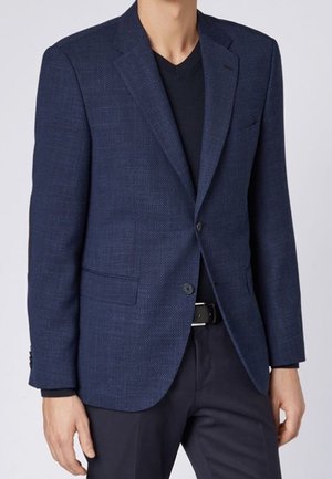 Blazer texturé bleu marine avec un col cranté, deux poches avant, fermeture à un bouton et doublure intérieure contrastante, associé à une chemise noire.