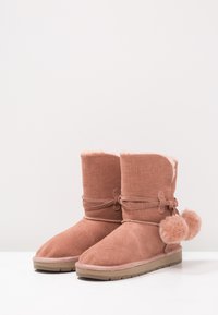 Růžové texturované ankle boots s umělým kožíškem, zavázané šňůrkou, se zdobným bambulí na boku a flexibilní gumovou podrážkou.
