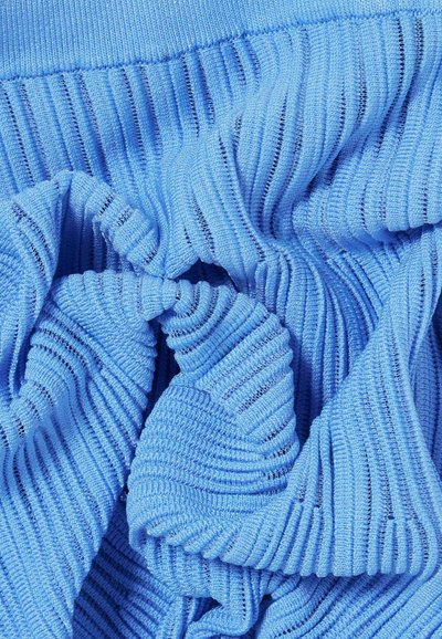 Tejido de ribete azul claro con líneas verticales prominentes, que presenta una textura suave y un ligero estiramiento, dispuesta de manera suelta y arrugada.