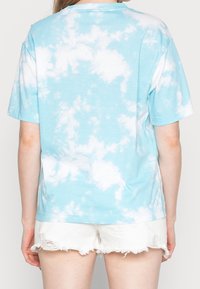 Jasnoniebieska koszulka w tye-dye o luźnym kroju, z krótkim rękawem i okrągłym dekoltem. Noszona z białymi, zniszczonymi szortami.