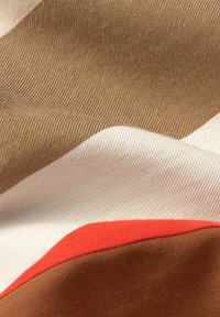 Tessuto multicolore con una texture ondulata. I colori includono marrone, bianco e un accento rosso brillante. La trama è liscia con una leggera lucentezza.