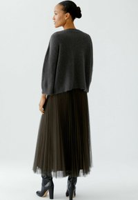 Gray knitted sweater with a loose fit, paired with a long, pleated tulle skirt in dark green, and knee-high black heeled boots.