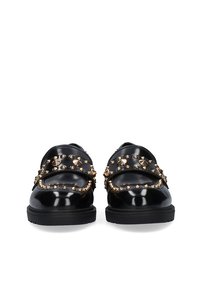 Zapatos de charol negro con correas adornadas con tachuelas doradas. Suela plana y diseño de punta redondeada. Presenta dos hebillas en la parte delantera.