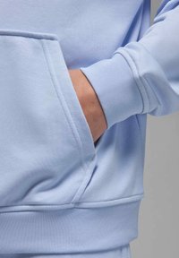 Sweatshirt azul claro com uma textura suave, apresentando um bolso canguru e punhos canelados. O tecido parece liso e elástico.