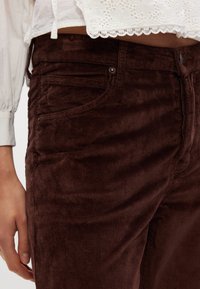 Bruine corduroy broek met smalle ribbels en een getailleerd ontwerp. De stof is textuurrijk, met voorzakken en een knoopsluiting.