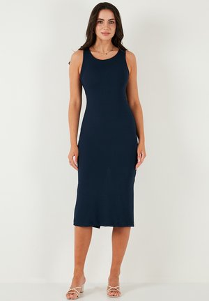 Abito midi senza maniche di colore blu navy in tessuto a costine, con silhouette aderente e scollatura rotonda, abbinato a sandali open-toe di colore chiaro.