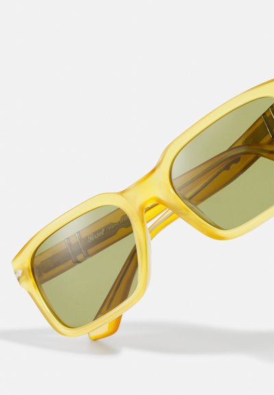 Ochelari de soare din plastic galben, cu un cadru rectangular masiv și lentile verzi. Prezintă inscripția "Persol" pe brațele interioare.
