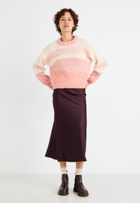 Maglione lavorato a maglia a righe rosa e crema, con un colletto a coste. Abbinato a una gonna di raso viola scuro e stivali ankle boots marroni.