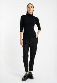 Czarna dopasowana bluzka z golfem i rękawami 3/4, zestawiona z dopasowanymi czarnymi spodniami i czarnymi platformami z frędzlami.