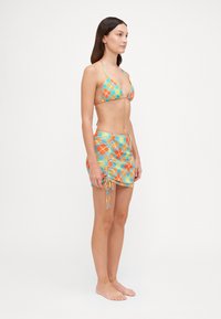Top bikini a triangolo in un vivace motivo blue, arancione e giallo; abbinato a una mini gonna coordinata con lacci laterali regolabili.