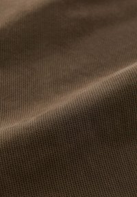 Tessuto testurizzato di colore marrone scuro, con un sottile motivo geometrico. La superficie è liscia con una leggera lucentezza, creando profondità visiva.