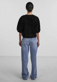 Fekete, textúrált, oversized pulóver rövid, puffos ujjakkal, magasan szabott, világoskék, széles nadrágokkal párosítva. Általában minimalista stílus.